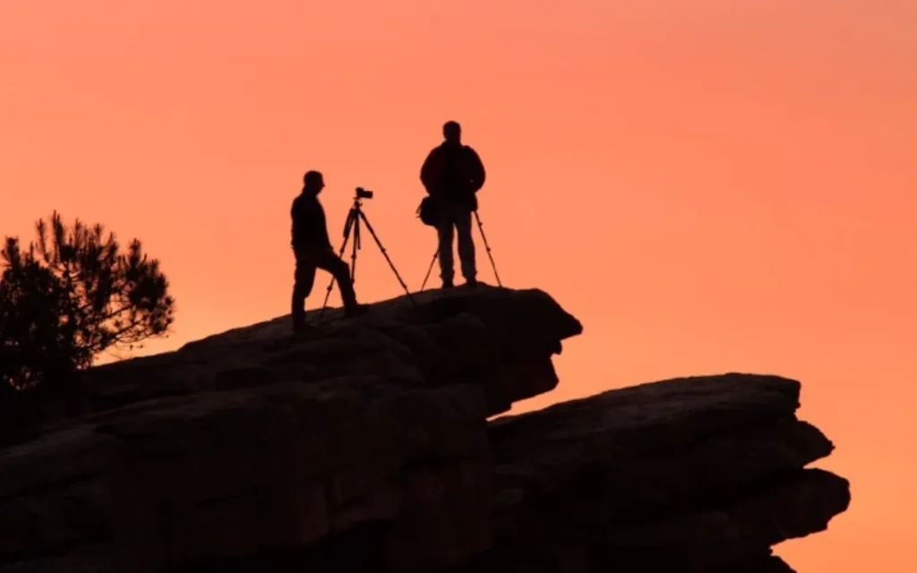 Silueta de dos personas con trípode frente a un atardecer naranja
